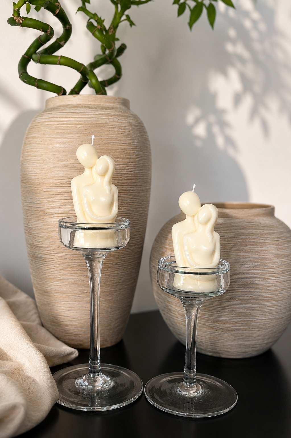 Zwei skulpturale Kerzen in Form einer innigen Umarmung auf eleganten Glasständern