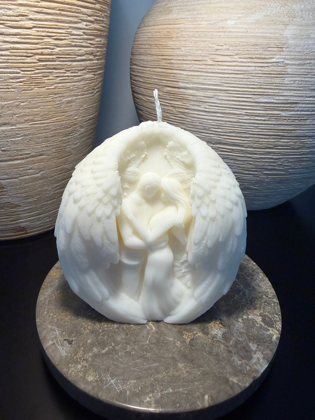 Handgefertigte weiße Kugelkerze mit Flügelmotiv auf Marmorplatte.